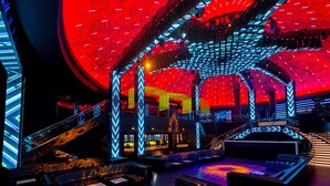 Un espacio moderno con un escenario central, zonas de estar y un diseño de techo geométrico distintivo.