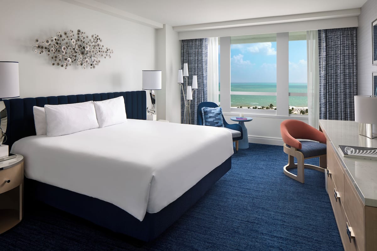 A hotel room with a large bed, a desk, a chair, and a view of the ocean.