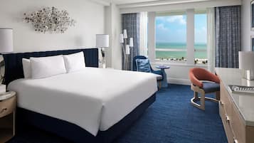 A hotel room with a large bed, a desk, a chair, and a view of the ocean.