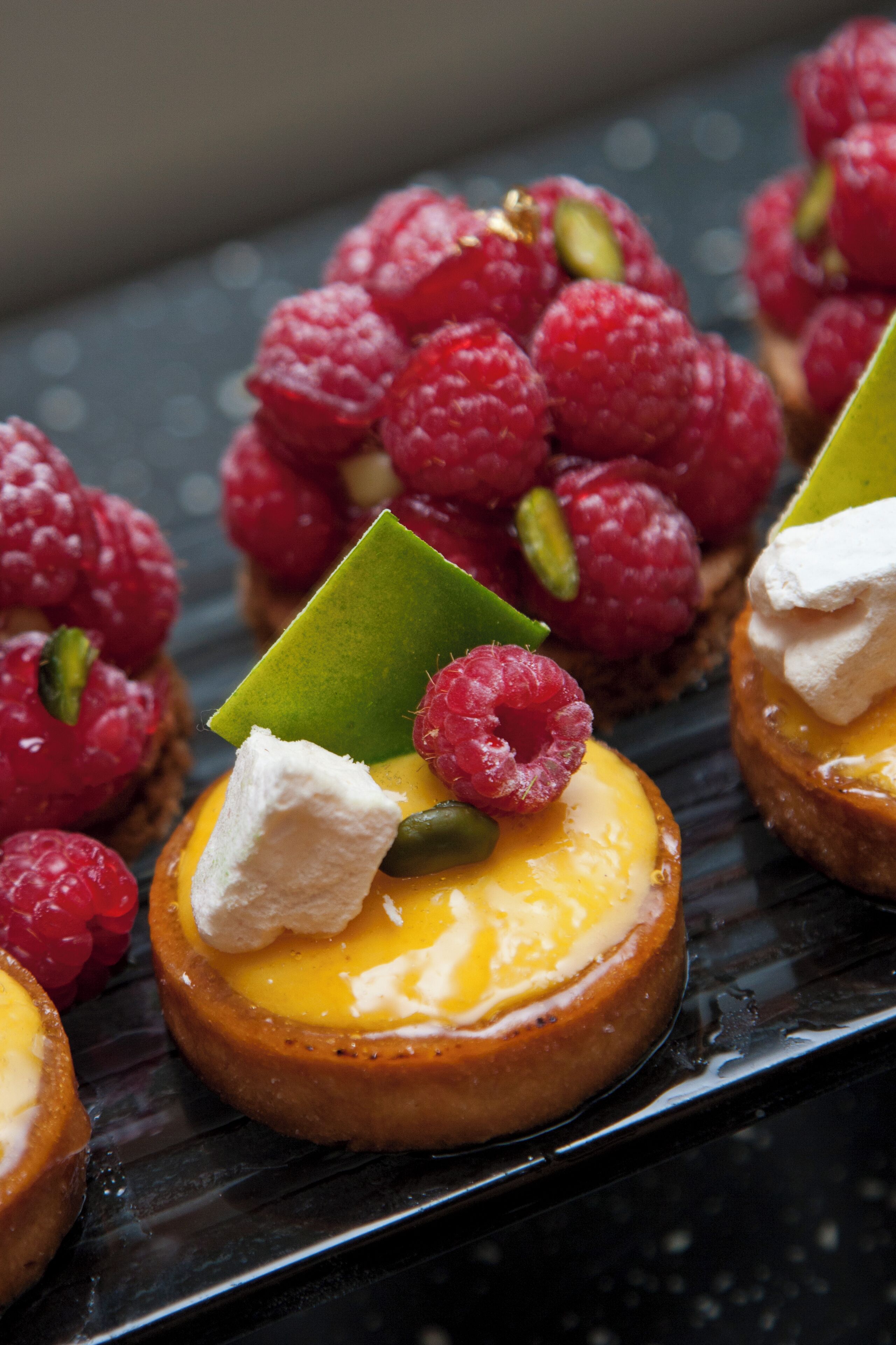 A dessert plate with small tarts topped with cream and raspberries.