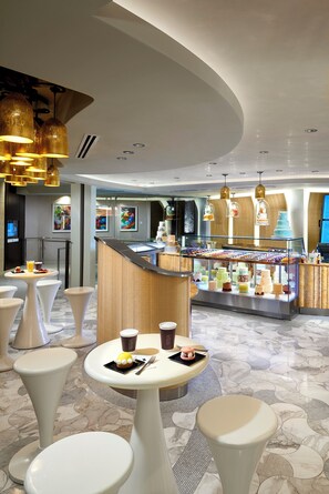 A modern hotel lobby with round tables, a dessert display, and a seating area.