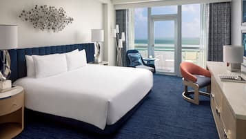 Quarto de hotel com uma cama grande, uma escrivaninha com cadeira, vista para o oceano e uma varanda.
