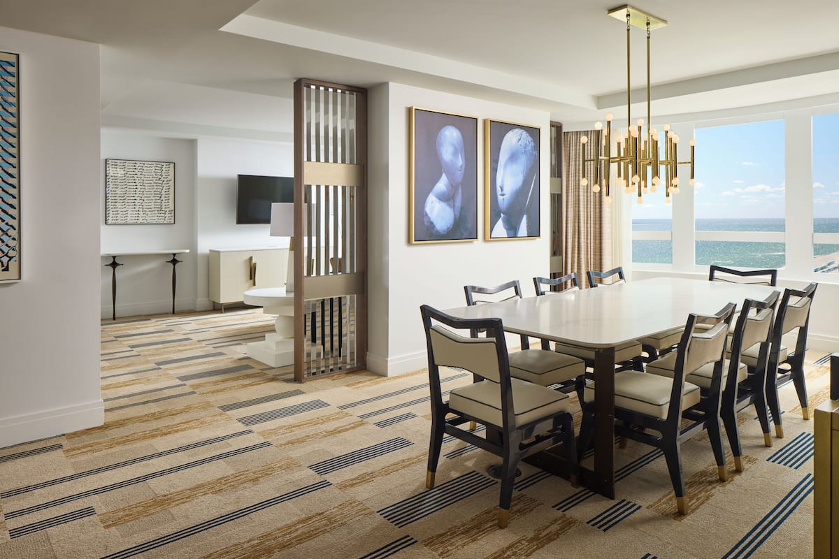 A dining area with a large table and chairs, a chandelier, and artwork on the walls.