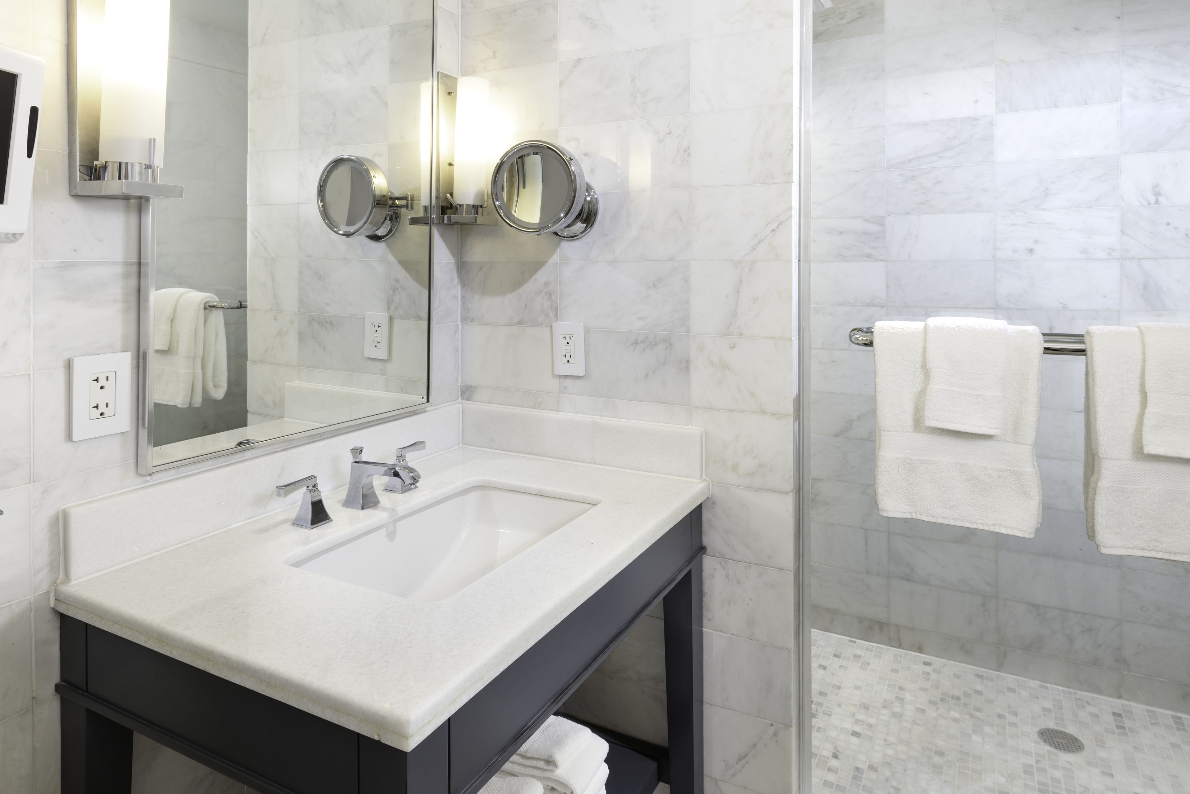 A modern bathroom with a large mirror, two sinks, and a shower area.