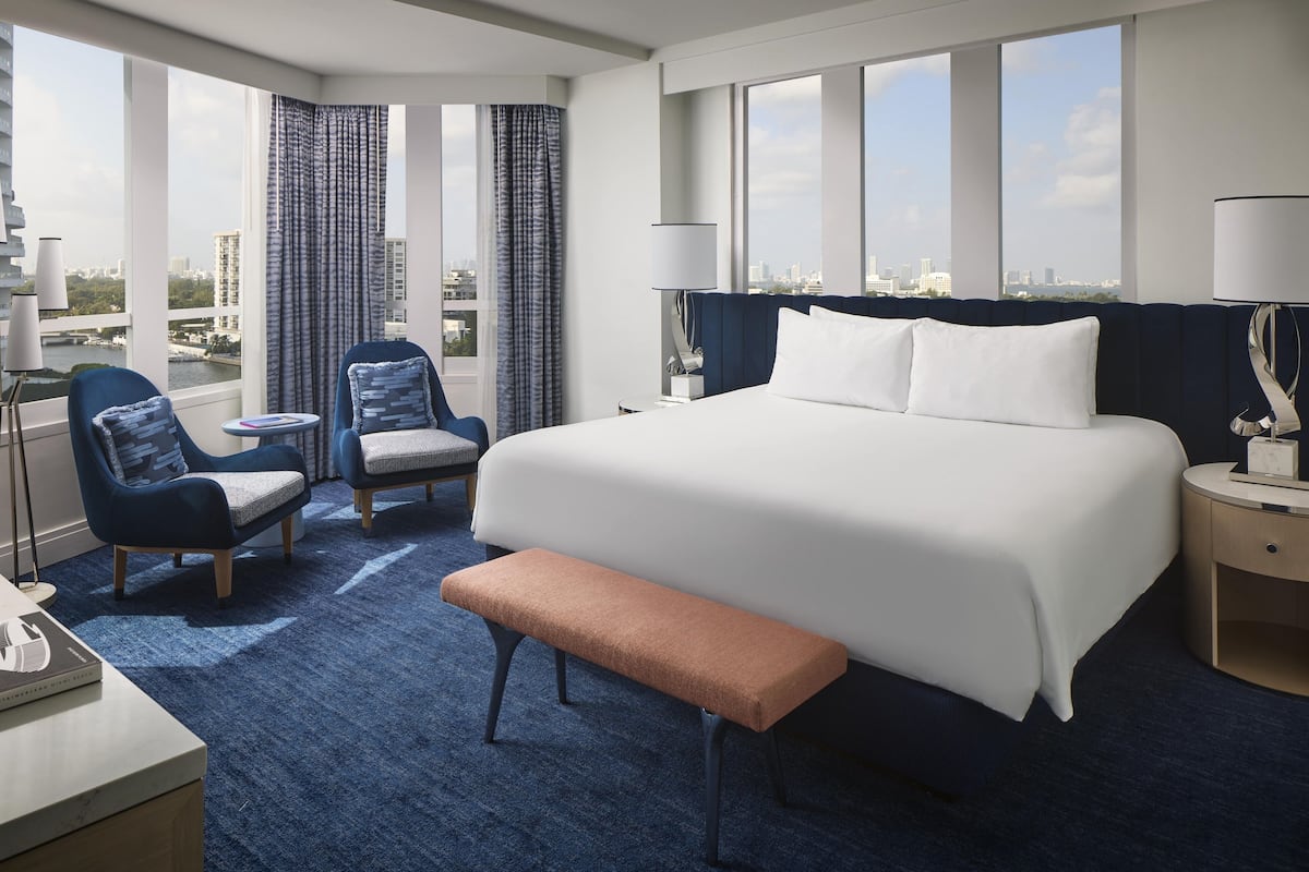 A hotel room with a large bed, two armchairs, a bench, a desk, and a lamp.