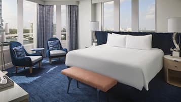 A hotel room with a large bed, two armchairs, a bench, a desk, and a lamp.