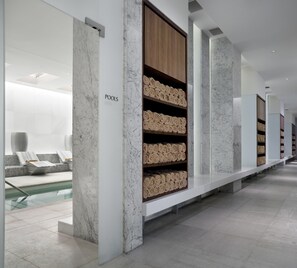 A modern spa area with a marble reception desk, a pool, and shelves with rolled towels.