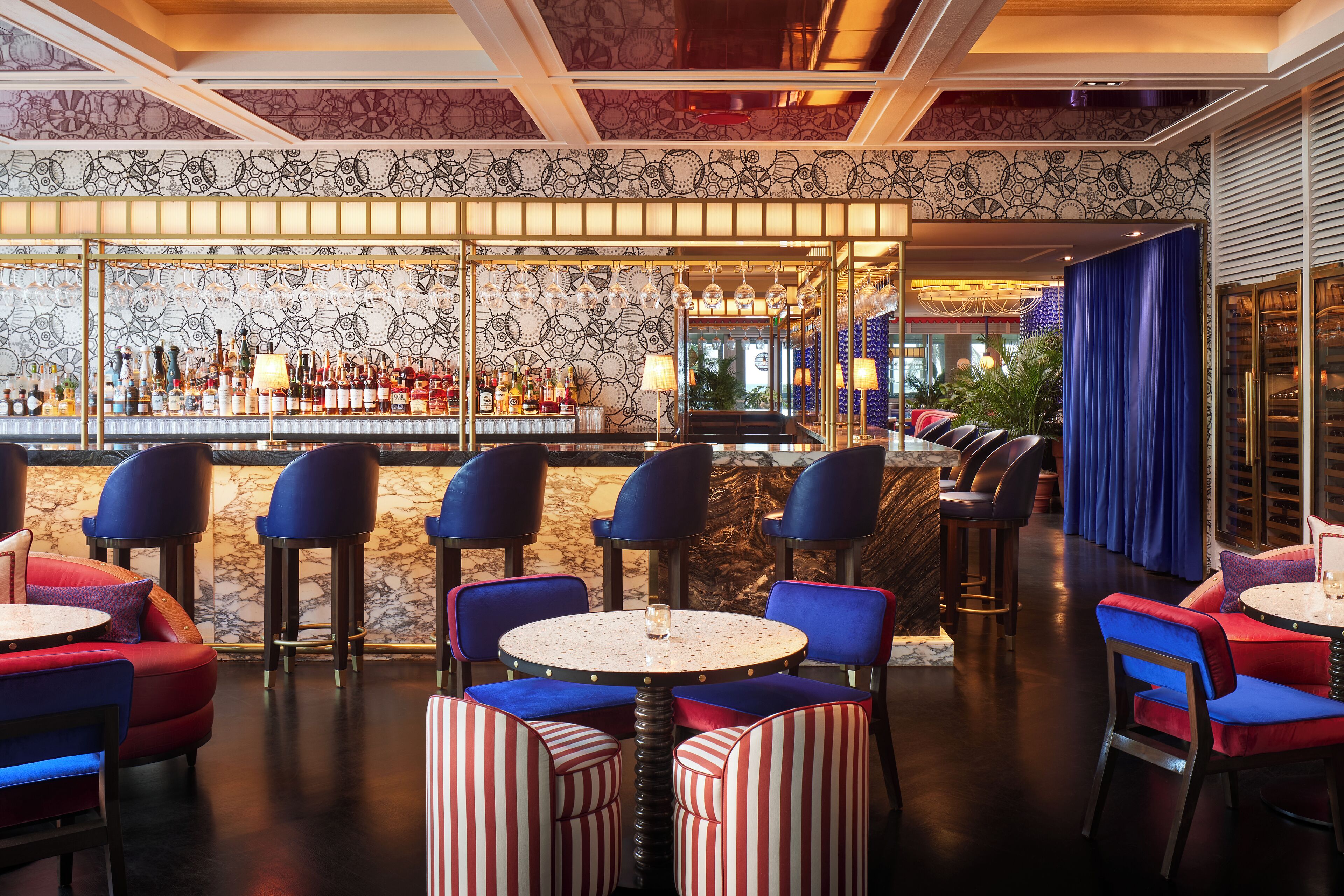 A bar area with round tables and chairs, a patterned wall, and a view of the bar.