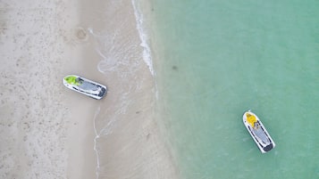 Vista aérea de una playa con dos barcos, una orilla arenosa y agua turquesa cristalina.