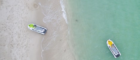 An aerial view of a beach with two boats, a sandy shore, and clear turquoise water.
