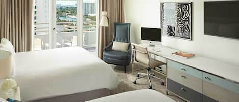 Habitación de hotel con dos camas, un escritorio con computadora, una silla, un televisor y vistas a la ciudad.