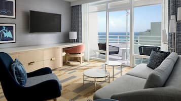 A modern hotel room with a sofa, armchair, small round table, and a TV mounted on the wall.