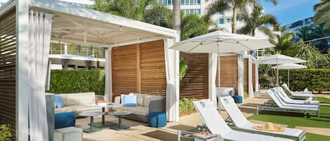 A poolside area with lounge chairs, a covered seating area with a sofa, and a building in the background.