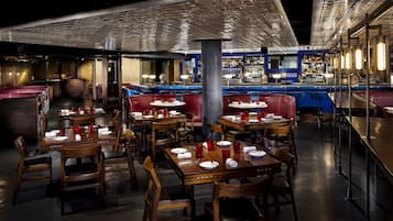 A restaurant with wooden tables and red upholstered booths, a bar area with bottles, and a patterned ceiling.
