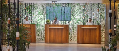 Un área de recepción con tres mostradores de madera, un mural grande en la pared y plantas en macetas.