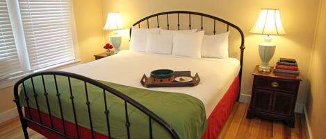 A neatly made bed with a green and red bedspread, two bedside tables with lamps, and a window with blinds.