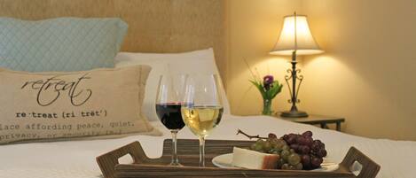 A bed with a tray containing two glasses of wine, a plate of cheese, and grapes.