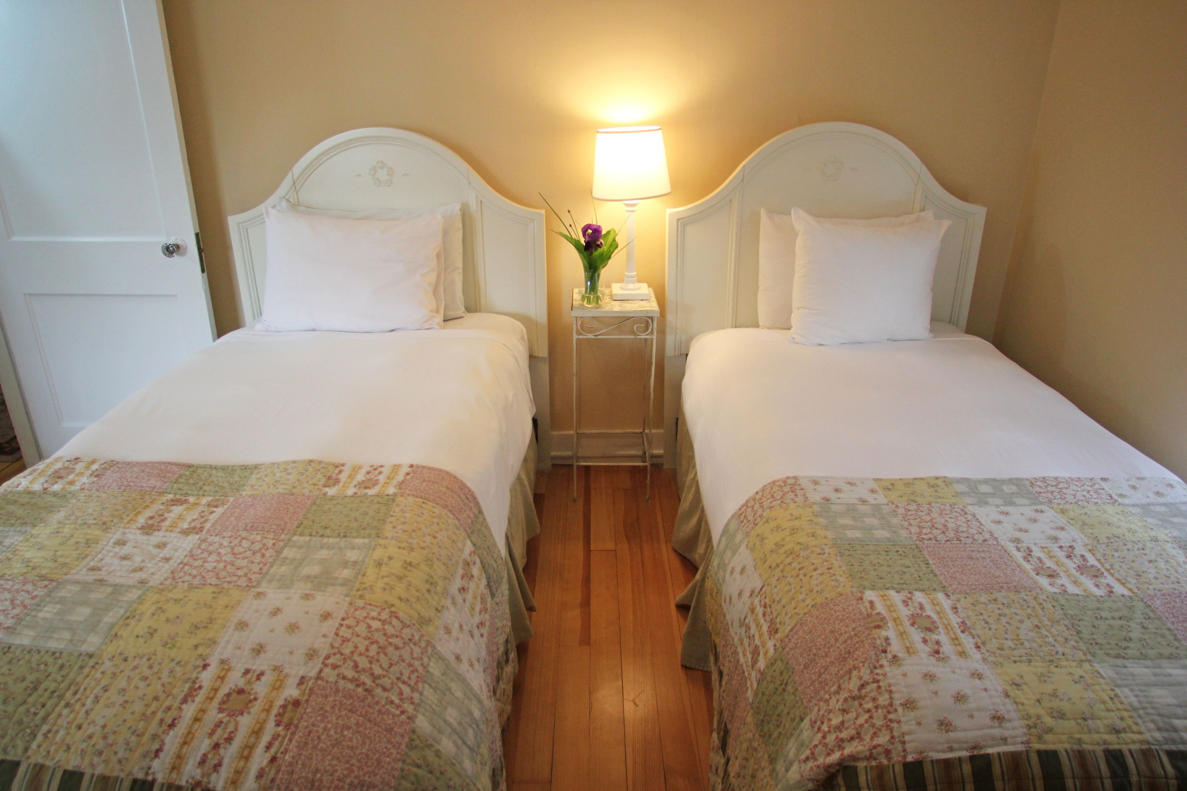 A hotel room with two beds, a nightstand with a lamp, and a door.