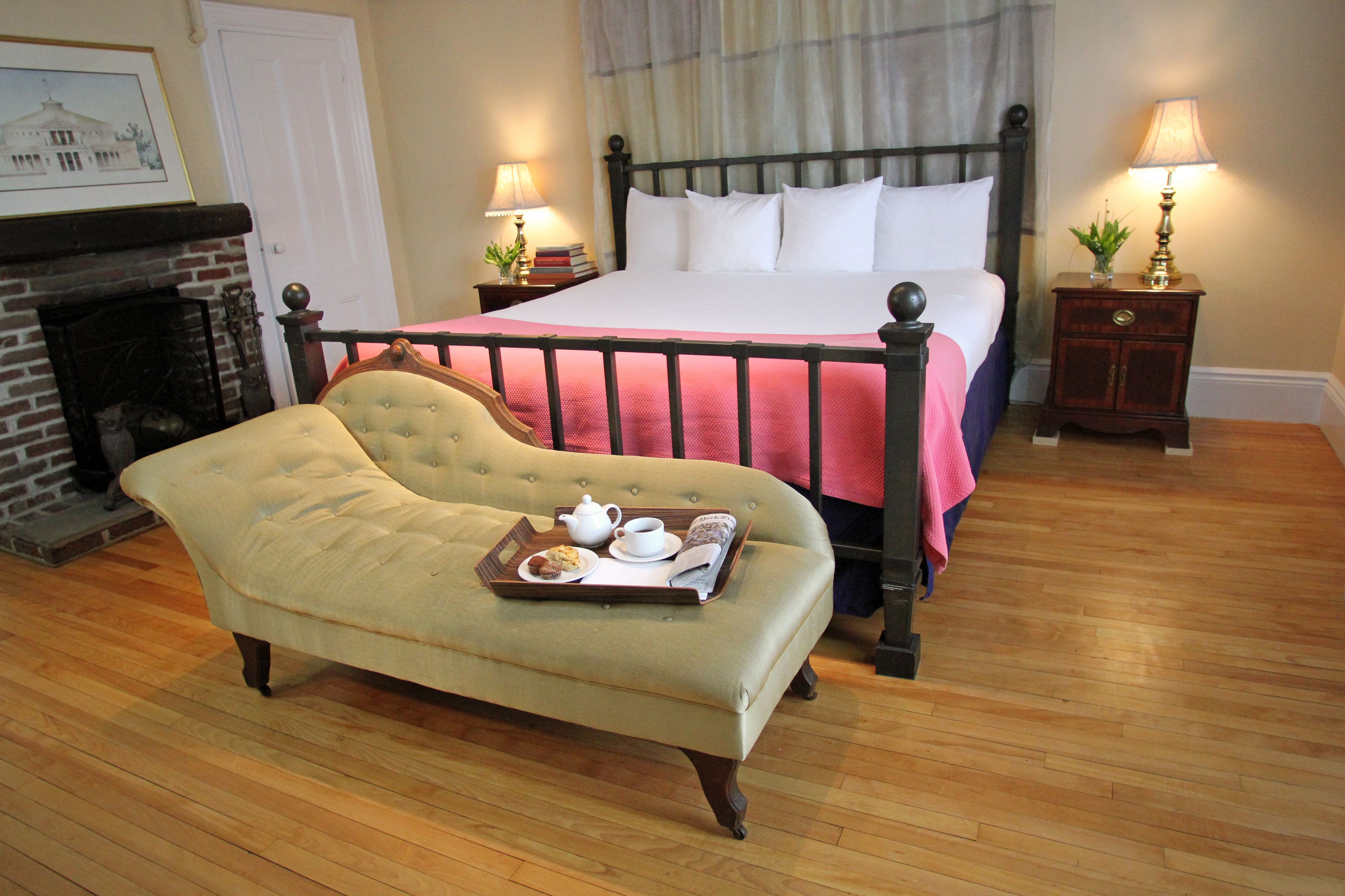 A bedroom with a bed, a bench with breakfast items, a fireplace, and two bedside tables with lamps.