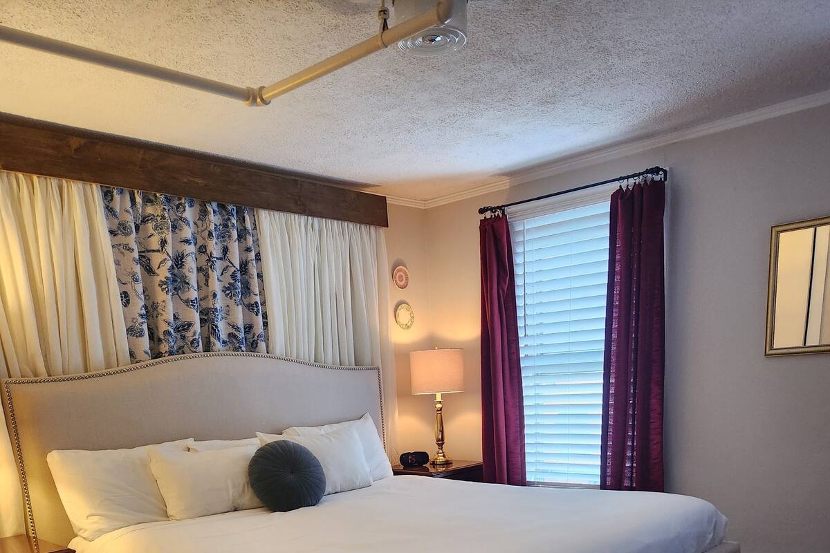 A neatly made bed with a headboard, a bedside table with a lamp, and a patterned rug on a wooden floor.