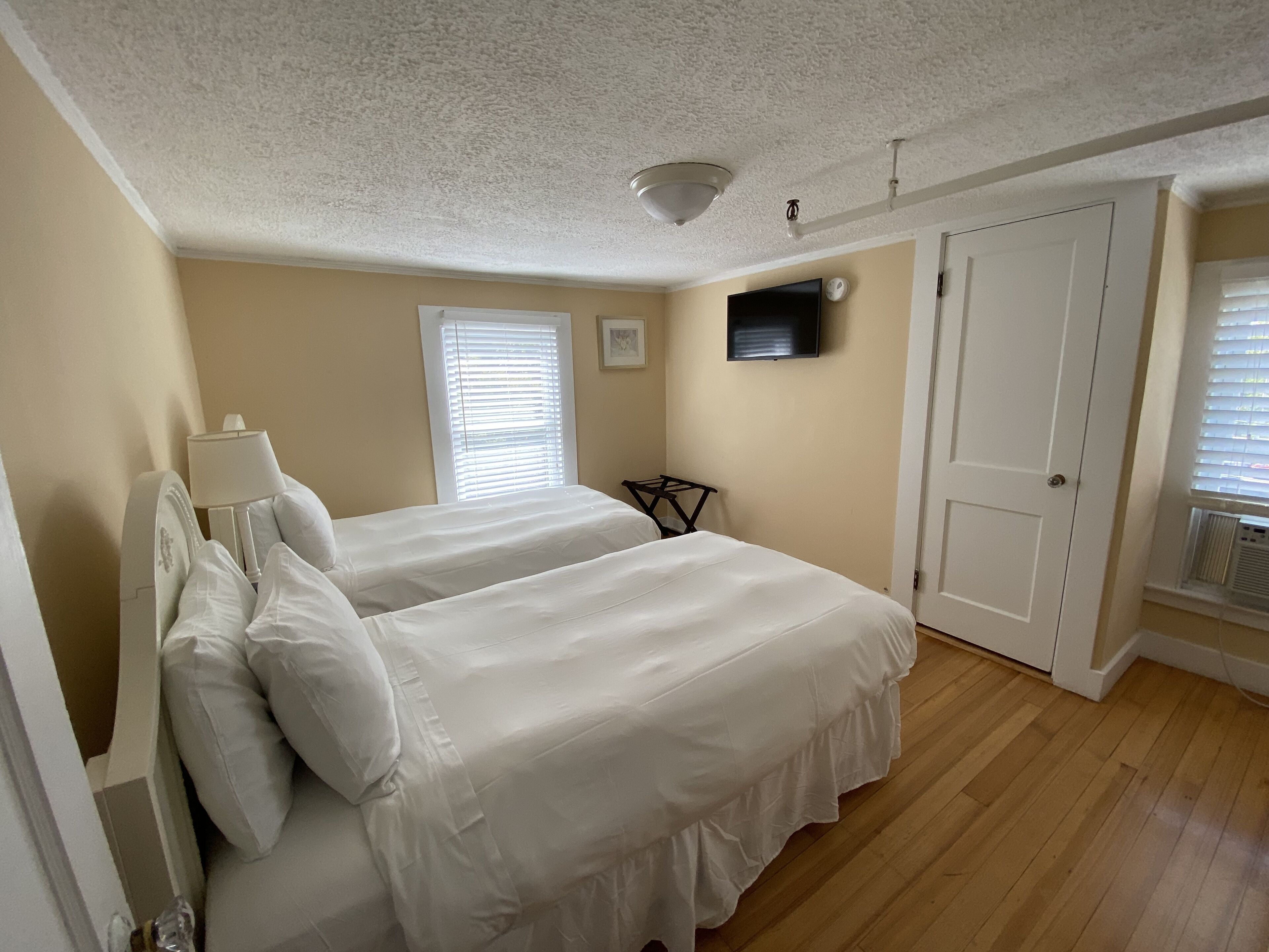 Une chambre avec deux lits, un ventilateur de plafond, une télévision et une porte.