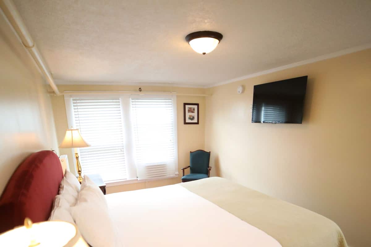 A hotel room with a bed, a lamp, a chair, and a television on the wall.