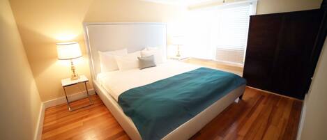 Une chambre à coucher avec un lit, des lampes de chevet, une fenêtre avec des stores et un plancher en bois.
