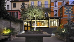 Un patio con un macetero central, un edificio moderno con ventanas amplias y un muro de ladrillo.