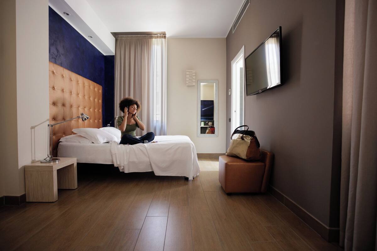 A hotel room with a large bed, a bedside table, a mirror, a TV mounted on the wall, and a suitcase on a chair.