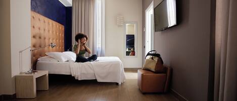 A hotel room with a large bed, a bedside table, a mirror, a TV mounted on the wall, and a suitcase on a chair.