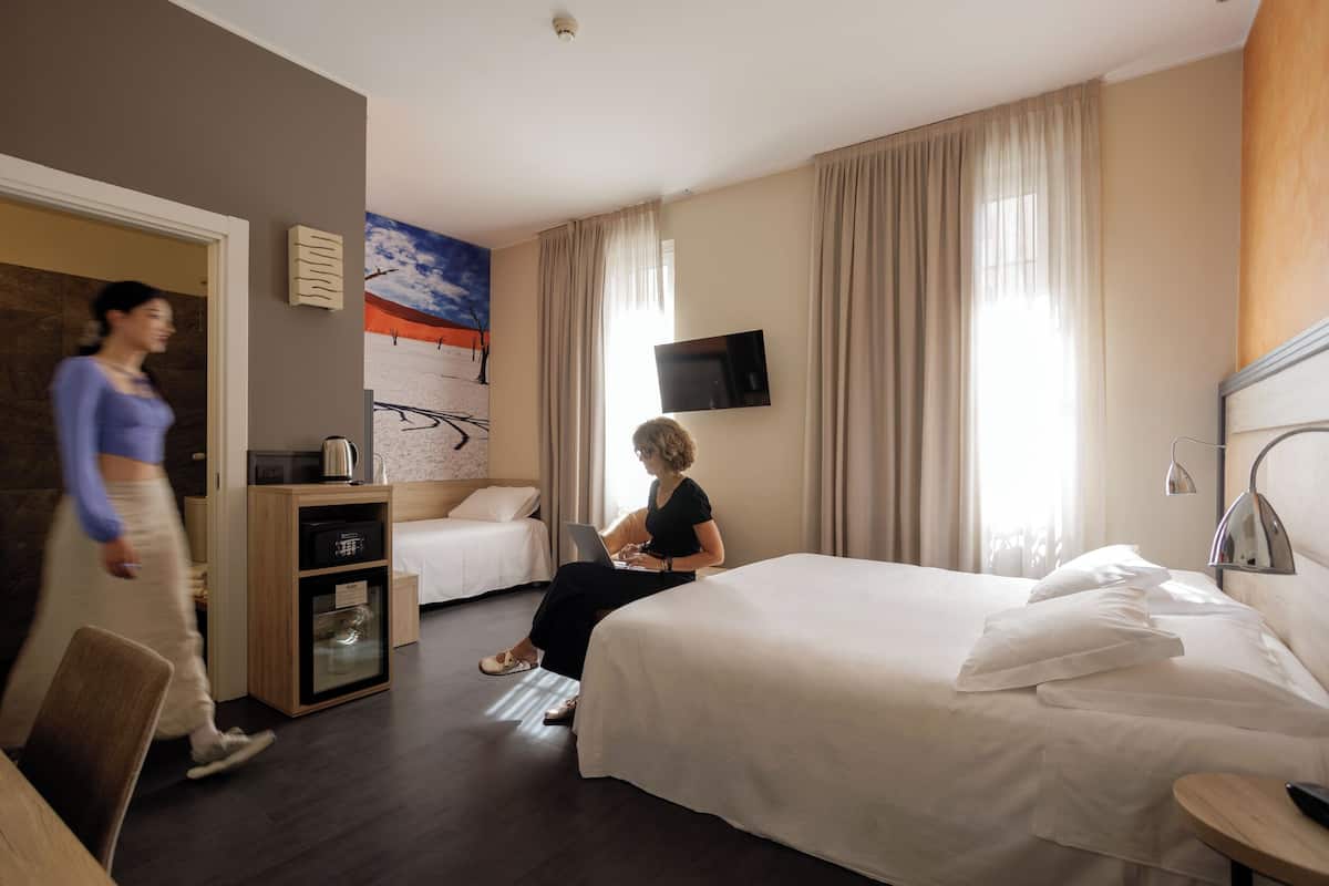 A hotel room with a bed, a desk, a television, and a painting on the wall.