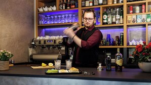 Un espace bar équipé d’une machine à café, d’étagères remplies de bouteilles et de verres, ainsi que d’un comptoir où sont disposés des aliments et des condiments.