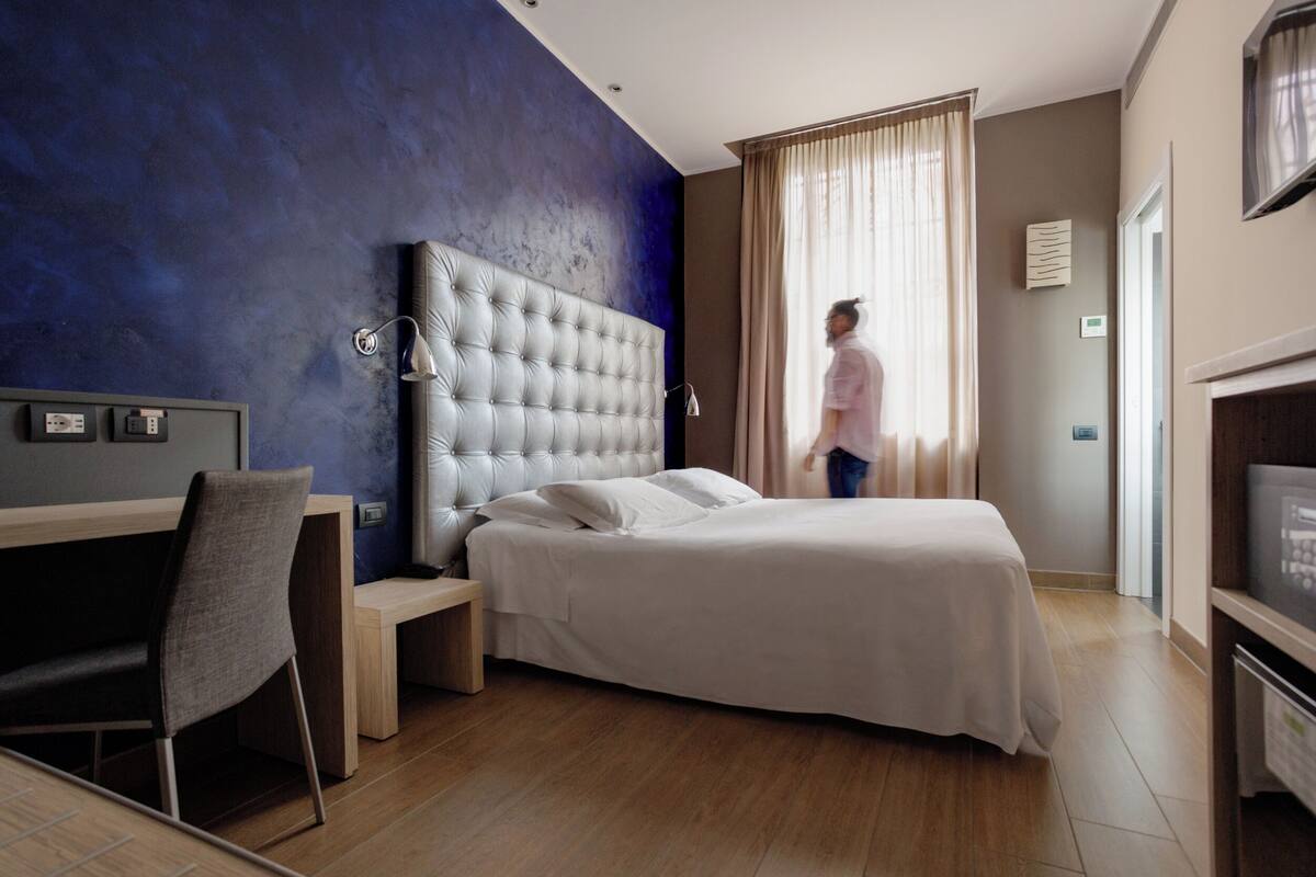 A modern hotel room with a large bed, a desk, and a TV.