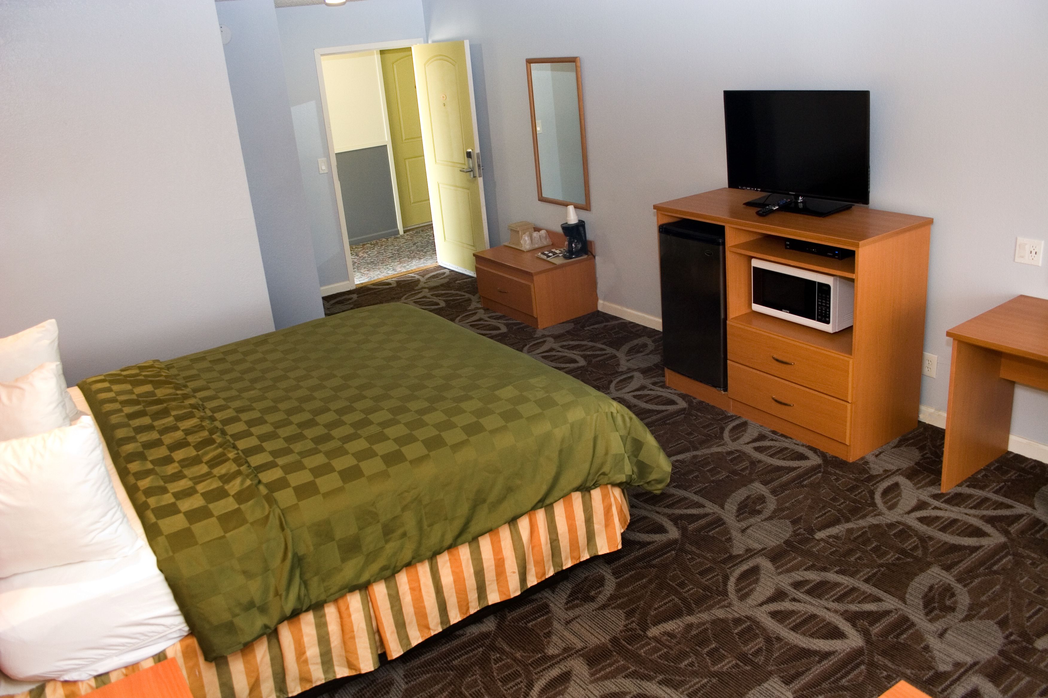 A hotel room with a bed, a desk, a television, a microwave, and a wardrobe.
