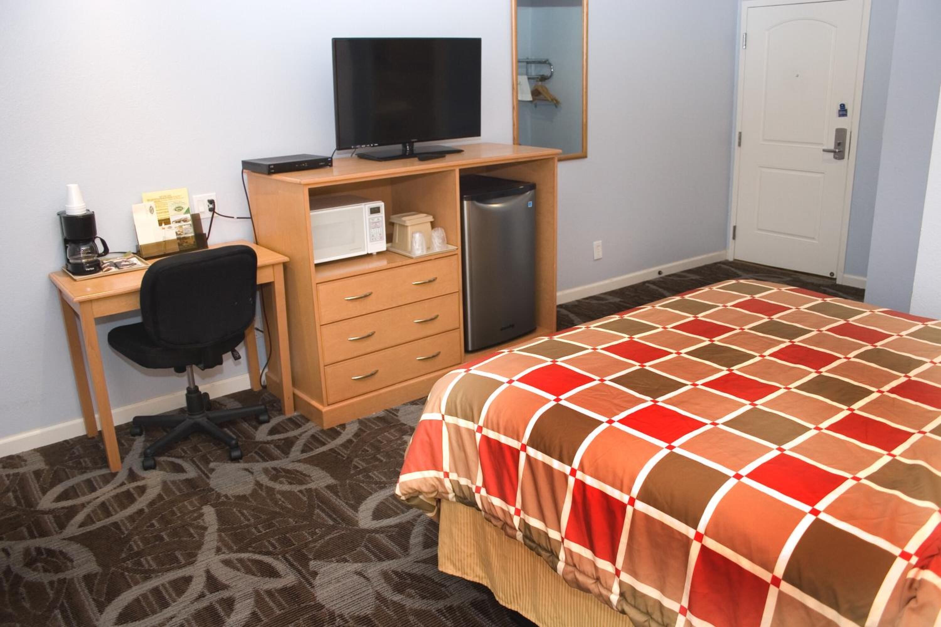 Une chambre d’hôtel équipée d’un lit, d’un bureau avec un ordinateur, d’une chaise, d’une machine à café, d’un four à micro-ondes et d’un réfrigérateur.