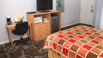 Une chambre d’hôtel équipée d’un lit, d’un bureau avec un ordinateur, d’une chaise, d’une machine à café, d’un four à micro-ondes et d’un réfrigérateur.