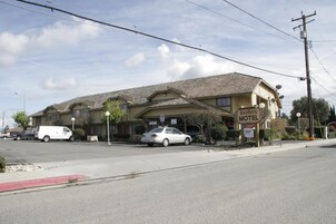 Um motel com estrutura em dois andares, estacionamento e vista para a rua.