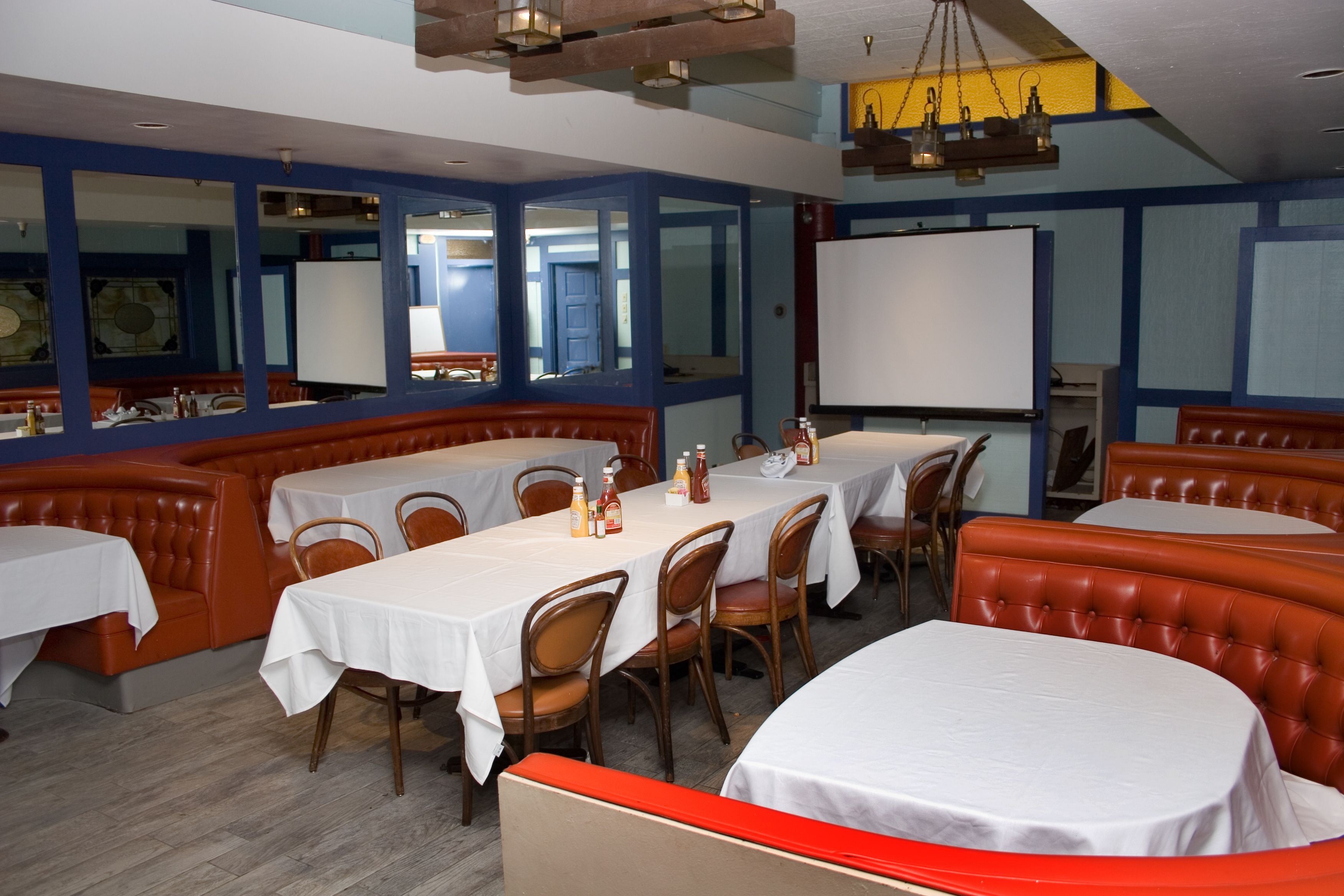 A restaurant with booths and tables, wooden chairs, and a whiteboard on the wall.