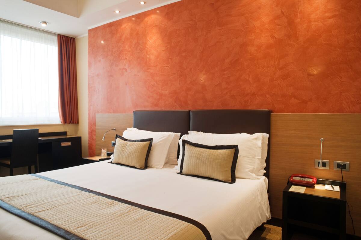 Ein Hotelzimmer mit einem großen Bett, zwei Nachttischen, einem Schreibtisch und einem Sessel.