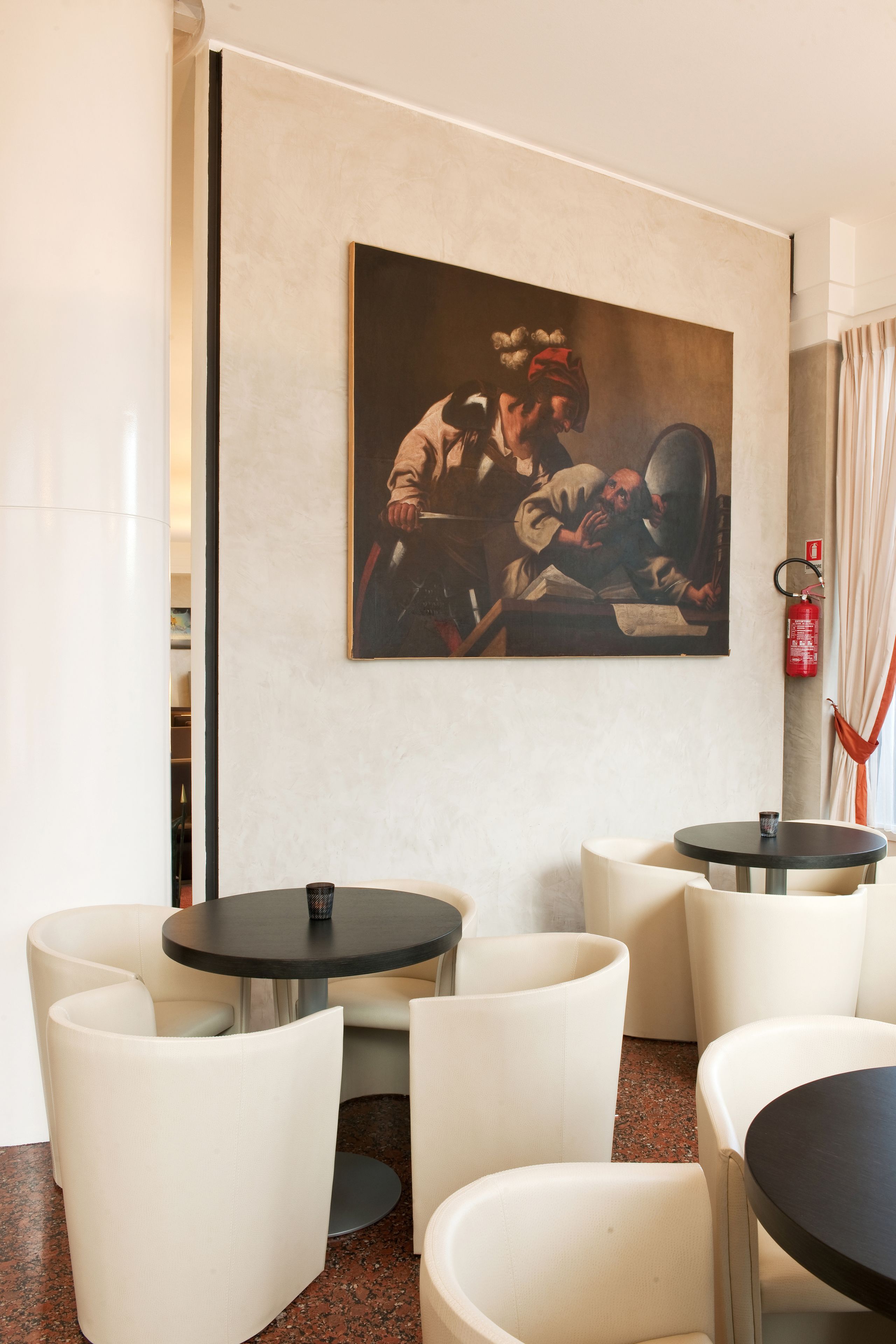 Een modern interieur met een schilderij, ronde tafels en witte stoelen.