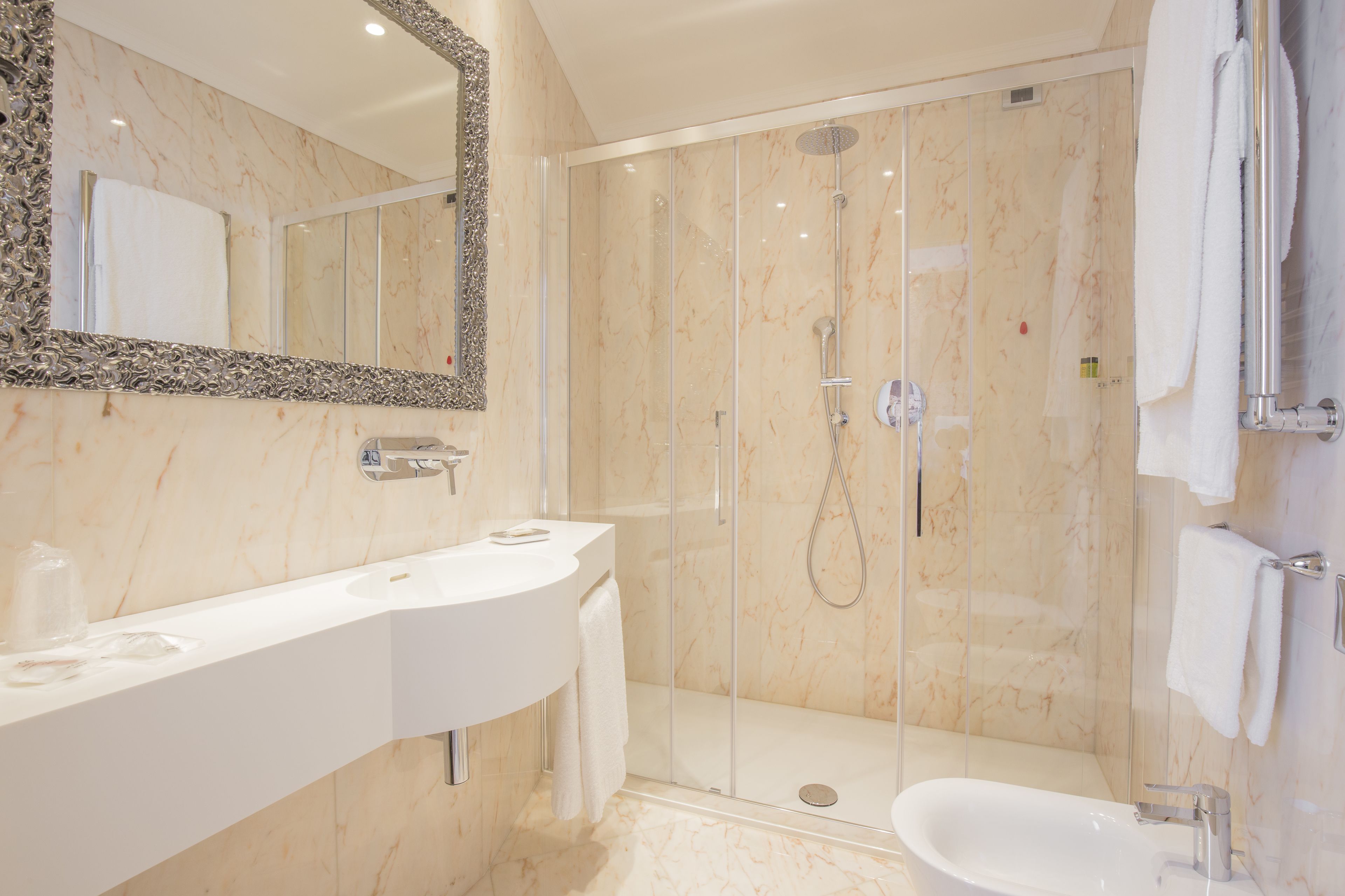 Een moderne badkamer met een marmeren wastafel, een douche met glazen wanden en een grote spiegel.