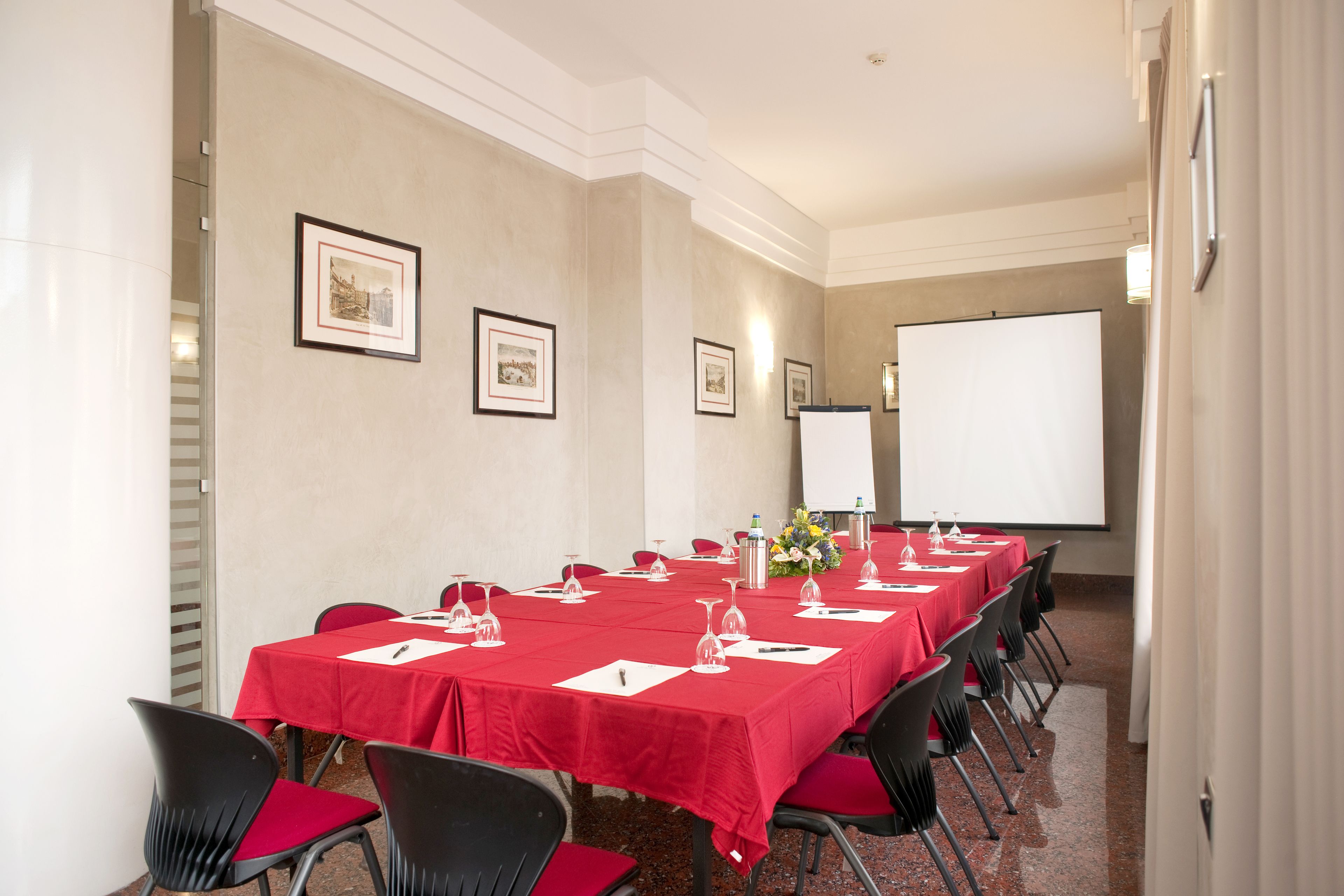 Una sala conferenze con un lungo tavolo, tovaglie rosse, sedie nere e una lavagna.