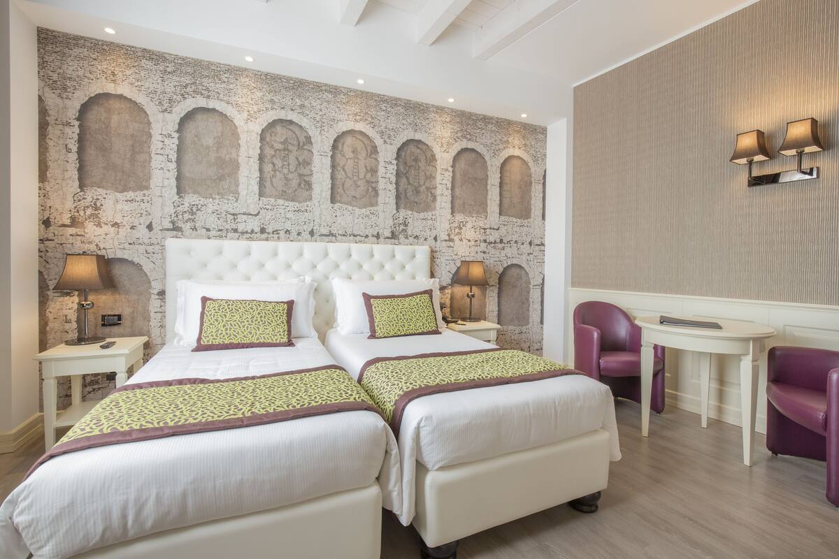 Ein Hotelzimmer mit zwei Betten, einem großen Bogenfenster, einem kleinen Tisch und zwei Stühlen.