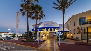 A hotel entrance with a blue and white awning, palm trees, and a clear sky. - Apartamentos Globales Binimar (Ciutadella de Menorca)