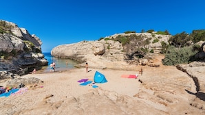 A beach with rocky terrain, clear blue sky, and people enjoying the water. - Apartamentos Globales Binimar (Ciutadella de Menorca)