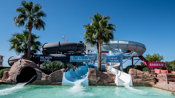 A water park with a large water slide, a black hole tunnel, and palm trees. - Apartamentos Globales Binimar (Ciutadella de Menorca)