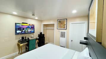 A hotel room with a bed, a desk with a computer, a TV mounted on the wall, a door, and a window.