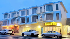 Un hotel de varios pisos con un llamativo letrero que dice "Ocean Inn", que presenta un diseño moderno con balcones y acceso a un garaje.