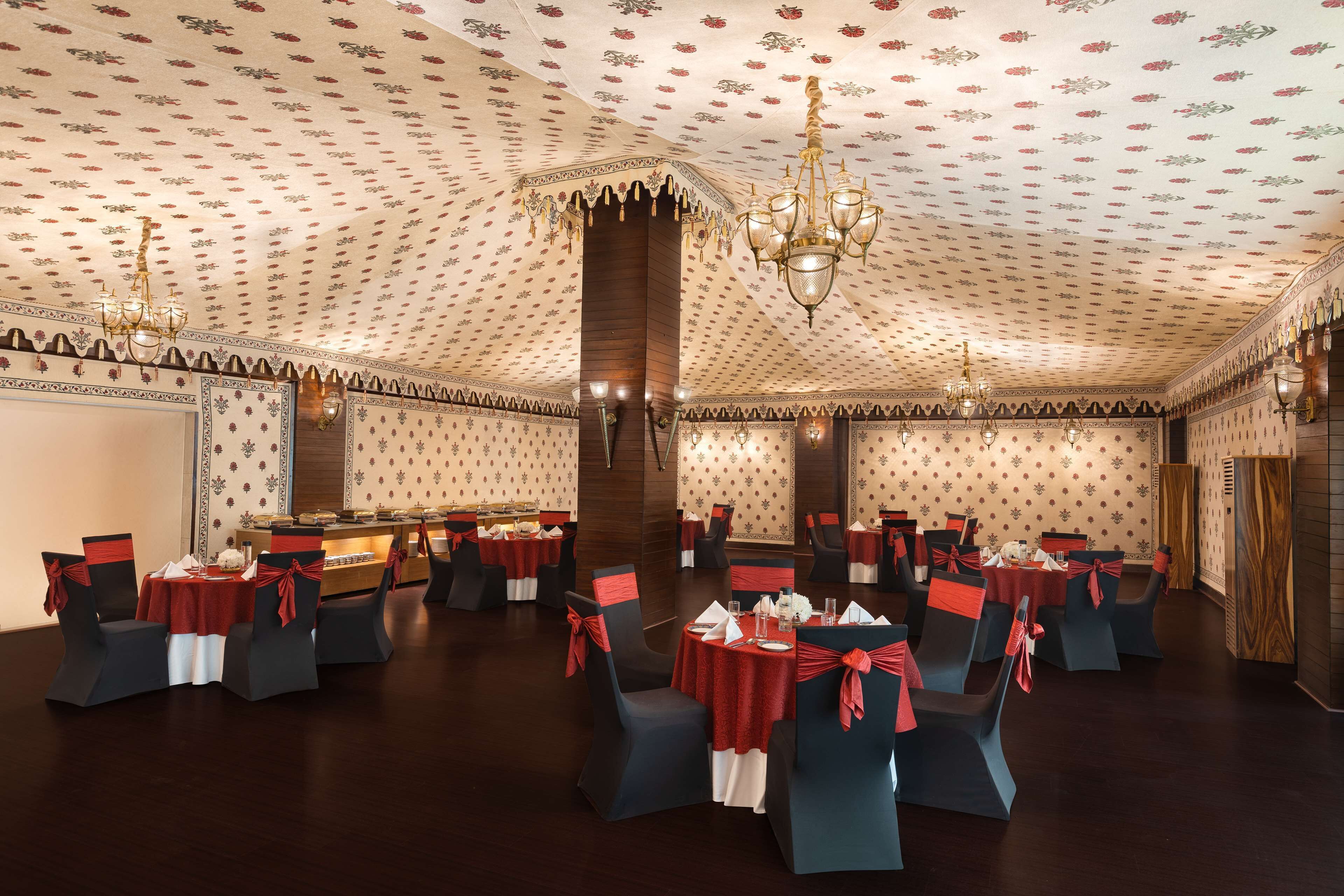 A banquet hall with round tables, dark chairs, and red tablecloths.
