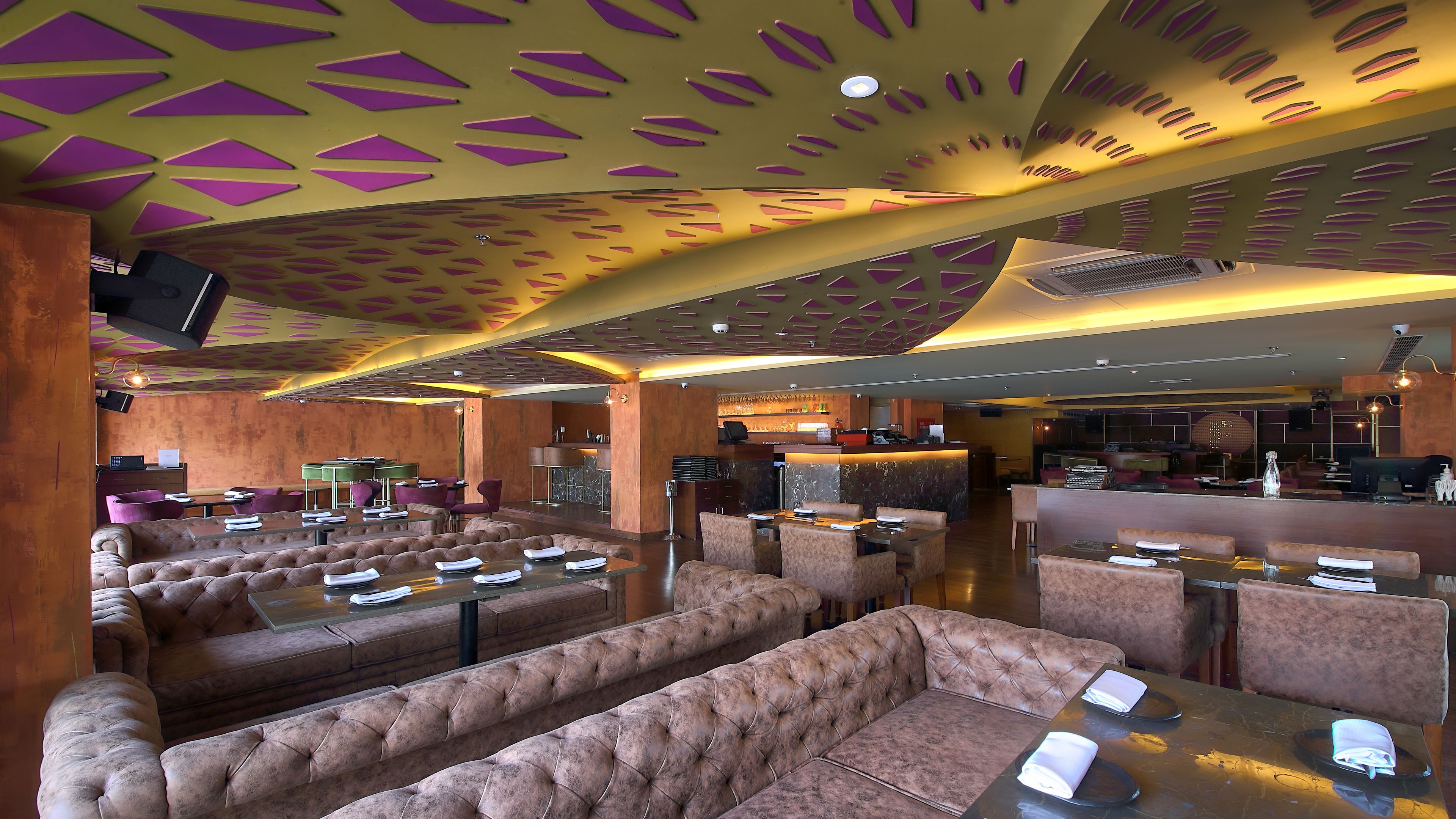 A restaurant with high-backed leather booths, a bar area, and a patterned ceiling.